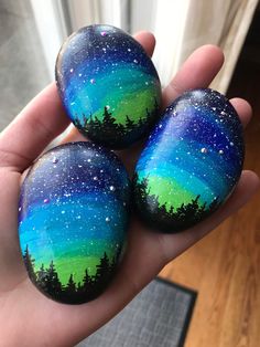 three painted rocks in the palm of someone's hand with trees and stars on them