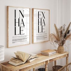 two framed posters on the wall above a table with books and plants in front of it