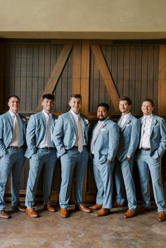 a group of men standing next to each other in front of a wooden wall wearing blue suits