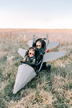 two people sitting in a buggy with an airplane on the back and one person wearing sunglasses