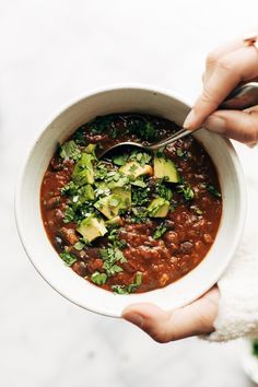 a person holding a bowl of chili with avocado