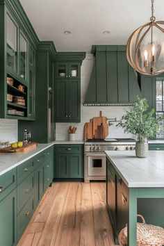 Modern kitchen with green cabinets, white countertops, and wooden floor, featuring a large island with a plant and a decorative light fixture. Green Kitchen Makeover, Green Kitchen Silver Hardware, Green Kitchen Cabinet Inspiration, Classic Kitchen Design Green, Dark Green Kitchen Units, Kitchen Forest Green, Green Kitchen Stainless Steel Appliances, Green Shades For Kitchen Cabinets, Artichoke Kitchen Cabinets