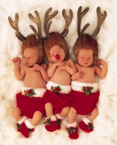 three babies dressed as santa claus and reindeers sleeping on a white fur covered surface