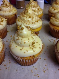 there are many cupcakes with white frosting and gold sprinkles