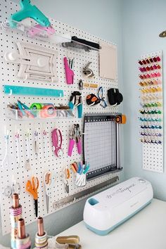 a white desk topped with lots of crafting supplies and scissors hanging on the wall