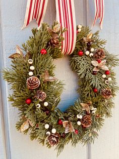 a christmas wreath hanging on a door with pine cones and berries around the wreath is decorated with red, white and gold ornaments