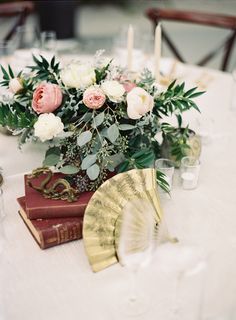 a table topped with books and flowers on top of a white table cloth covered table