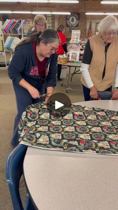 three women are looking at a quilt on a table