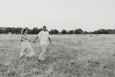 a man and woman holding hands walking through a field