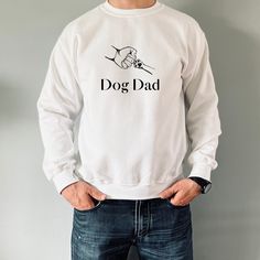 a man standing with his hands on his hips wearing a white dog dad sweatshirt and jeans