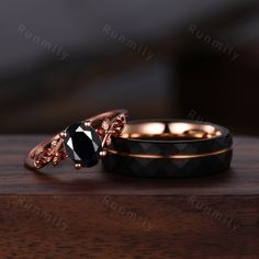 two wedding rings with black and rose gold accents on top of each other, sitting on a wooden surface