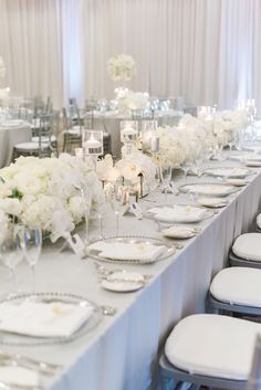 a long table is set with white flowers and place settings