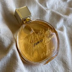 a bottle of perfume sitting on top of a white sheet with writing in gold ink