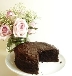 a piece of chocolate cake sitting on top of a white plate next to pink roses