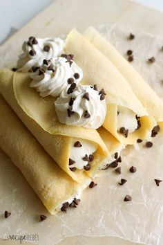 three crepes topped with whipped cream and chocolate chips on a piece of parchment paper