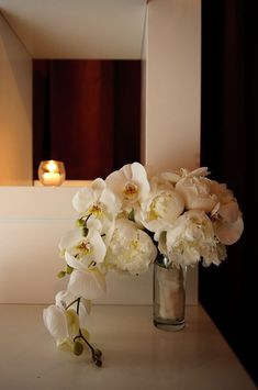 a vase filled with white flowers sitting on top of a counter next to a mirror