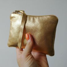 a hand holding a gold colored purse with an orange nail polish on the tip of it