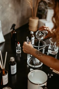 a person pouring something into a glass on top of a table with bottles and spoons