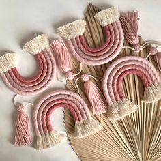 pink and white decorative items made out of wood sticks on a white surface with fringes