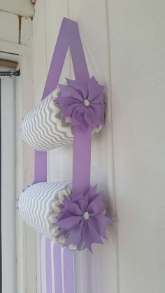 two decorative pillows hanging on the side of a white door with purple ribbons attached to them