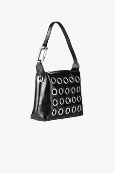 This version of the signature Slim Moon bag has been crafted in Italy from patent leather, it also features a cut-out front detail with metal eyelet. The top handle is accented with a snap hook that features a functioning hinge. Composition:100% Calf Leather & Metal Patches Made in Italy Colour: Black Hook:100% Eco Brass Hook SIZE & FIT Bag Dimensions: 18x15x6 cm EÉRA'S NOTE This bag turns out to be highly versatile and can match any type of outfit, from day to night. Modern Evening Bag With Hardware Details, Modern Evening Bag With Hardware, Modern Evening Bags With Hardware, Designer Shoulder Bag With Hardware For Evening, Metal Patches, Black Hook, Moon Bag, Brass Hook, Earring Necklace