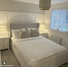 a bed with white sheets and pillows in a bedroom next to two lamps on either side of the bed