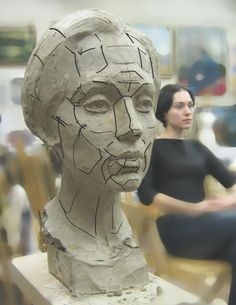 a woman sitting in front of a clay head on a wooden chair next to another person