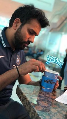 a man sitting at a table with a cup in his hand and writing on it