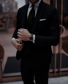 a man in a suit and tie standing by a glass door with his hands on his chest