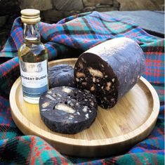 a bottle of whiskey and some food on a wooden plate next to a plaid blanket