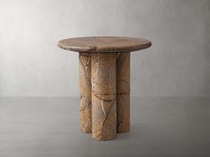 a round wooden table sitting on top of a cement floor next to a white wall