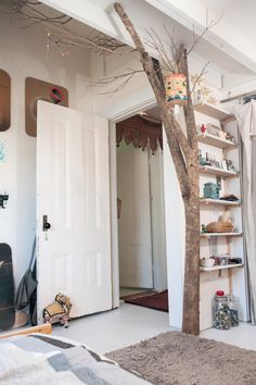 a tree in the corner of a room next to a bed and bookshelf