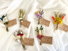 six different types of flowers are laid out on a white sheet, with tags attached to them