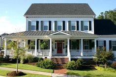 a large white house with black shutters on the front porch and red door, surrounded by lush green grass