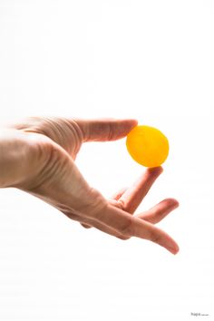 a person's hand holding an orange object in front of a white background,