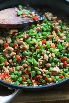 a skillet filled with green beans and meats on top of a wooden table