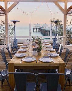 an outdoor dining table set with plates and place settings for dinner on a deck overlooking the ocean