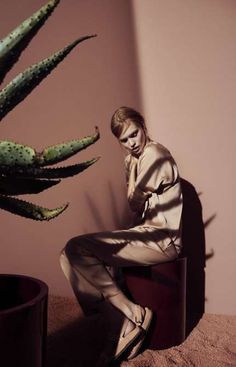 a woman sitting on a stool next to a cactus