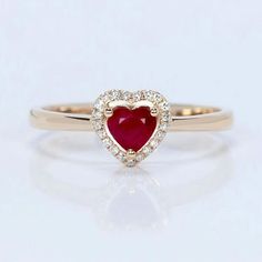 a gold ring with a heart shaped ruby and white diamonds in the middle, on a light background