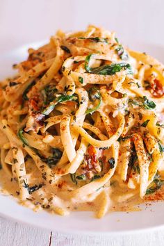 a white plate topped with pasta covered in sauce and spinach leafy garnish