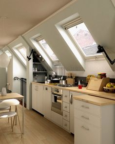 an attic kitchen with white cabinets and wooden flooring is shown in this image, there are skylights on the roof