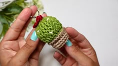 a person holding a small crocheted cactus ornament in their left hand