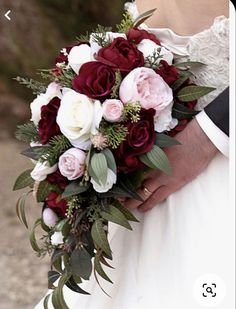 a close up of a person holding a wedding bouquet with red and white flowers on it