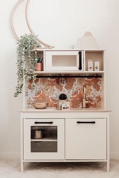 a white cabinet with an oven and microwave in it next to a potted plant