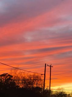 an orange and pink sky at sunset with power lines in the foreground, trees to the right