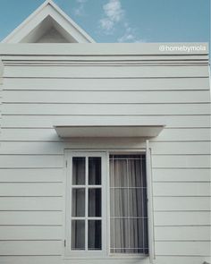 a cat sitting on the window sill of a white house with a blue sky in the background