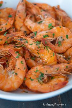 a white bowl filled with cooked shrimp and garnished with parsley on top