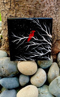 a red bird sitting on top of a black box next to rocks and a tree