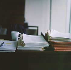 a stack of papers sitting on top of a wooden table next to a cup and saucer