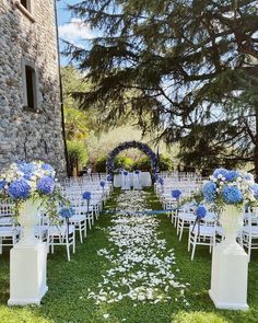 an outdoor ceremony set up with white chairs and blue flowers on the grass in front of a stone building